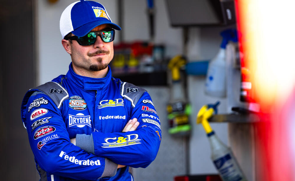 Logan Schuchart stands in his firesuit with sunglasses on