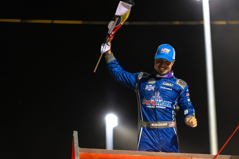 World of Outlaws Sprint Car Series driver Logan Schuchart with a checkered flag in his hand celebrating atop his car in Attica Raceway Park Victory Lane