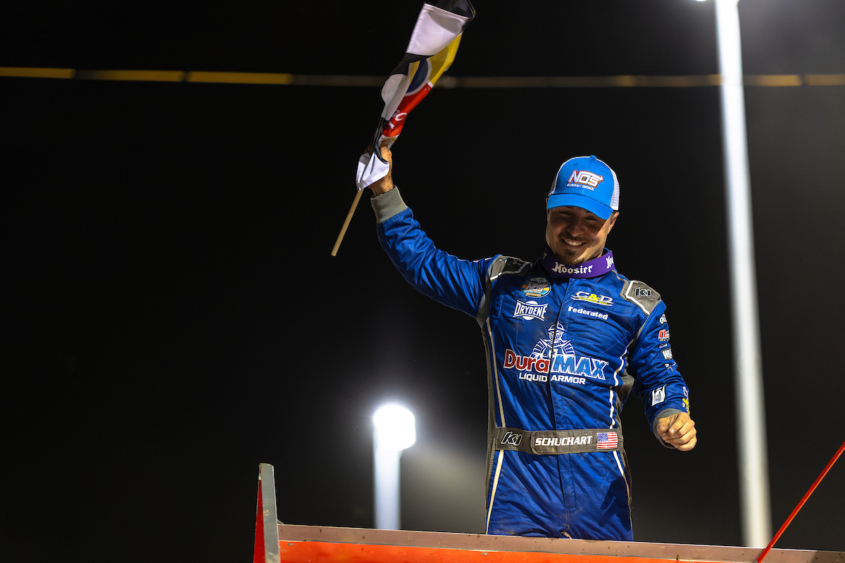 World of Outlaws Sprint Car Series driver Logan Schuchart with a checkered flag in his hand celebrating atop his car in Attica Raceway Park Victory Lane
